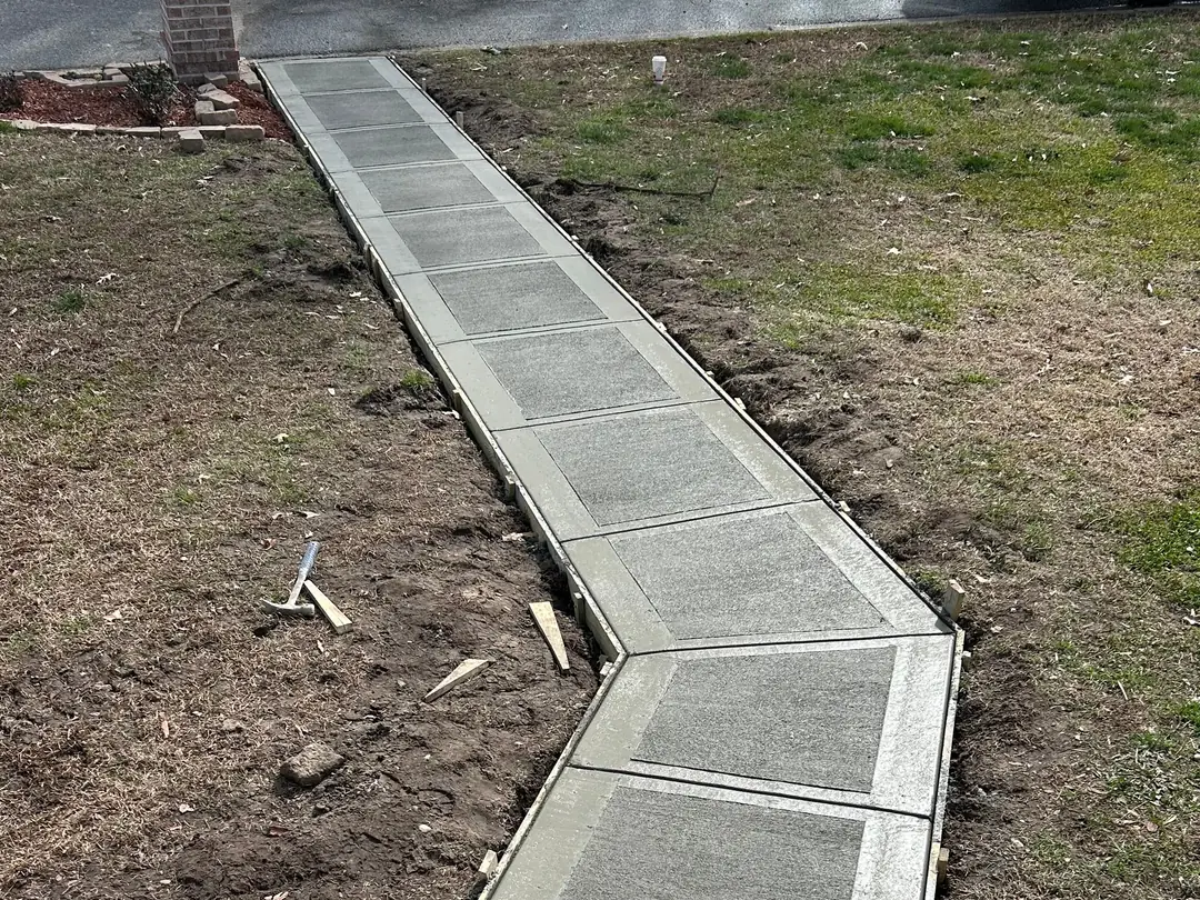 Newly installed concrete walkway with decorative borders and square-patterned sections extending through a residential yard