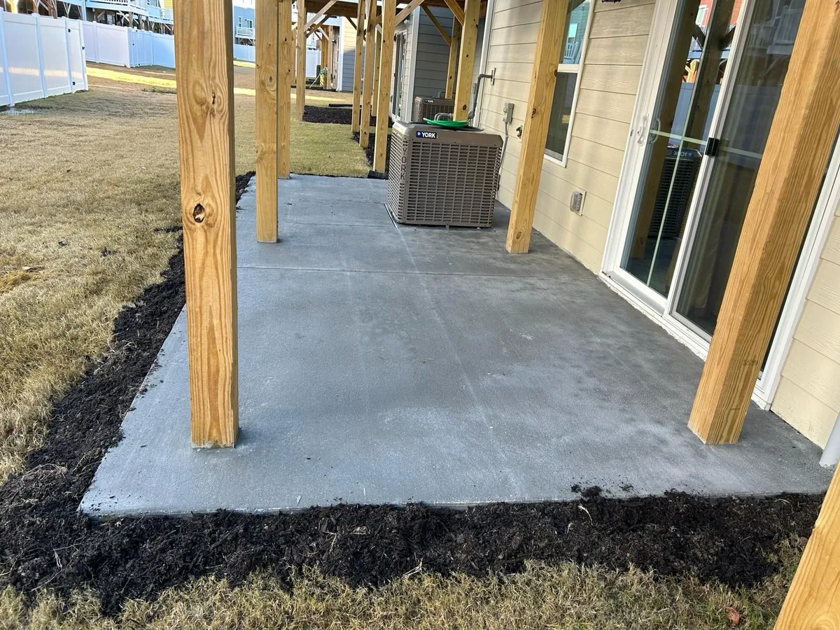 New concrete patio with wooden support posts next to a house exterior with sliding glass doors